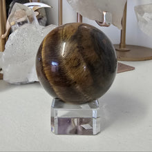 Load image into Gallery viewer, Tiger's eye crystal ball on a stand with crystals in the background