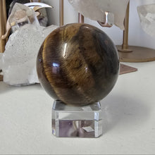 Load image into Gallery viewer, Tiger&#39;s eye crystal ball on a stand with crystals in the background
