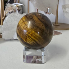 Load image into Gallery viewer, Tiger&#39;s eye crystal ball on a stand with crystals in the background
