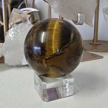 Load image into Gallery viewer, Tiger&#39;s eye crystal ball on a white surface with crystals in the background
