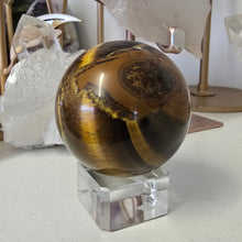 Load image into Gallery viewer, Tiger&#39;s eye crystal ball on a stand with crystals in the background
