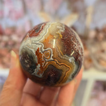 Load image into Gallery viewer, Hand holding a polished stone with brown, orange, and white patterns against a blurred background
